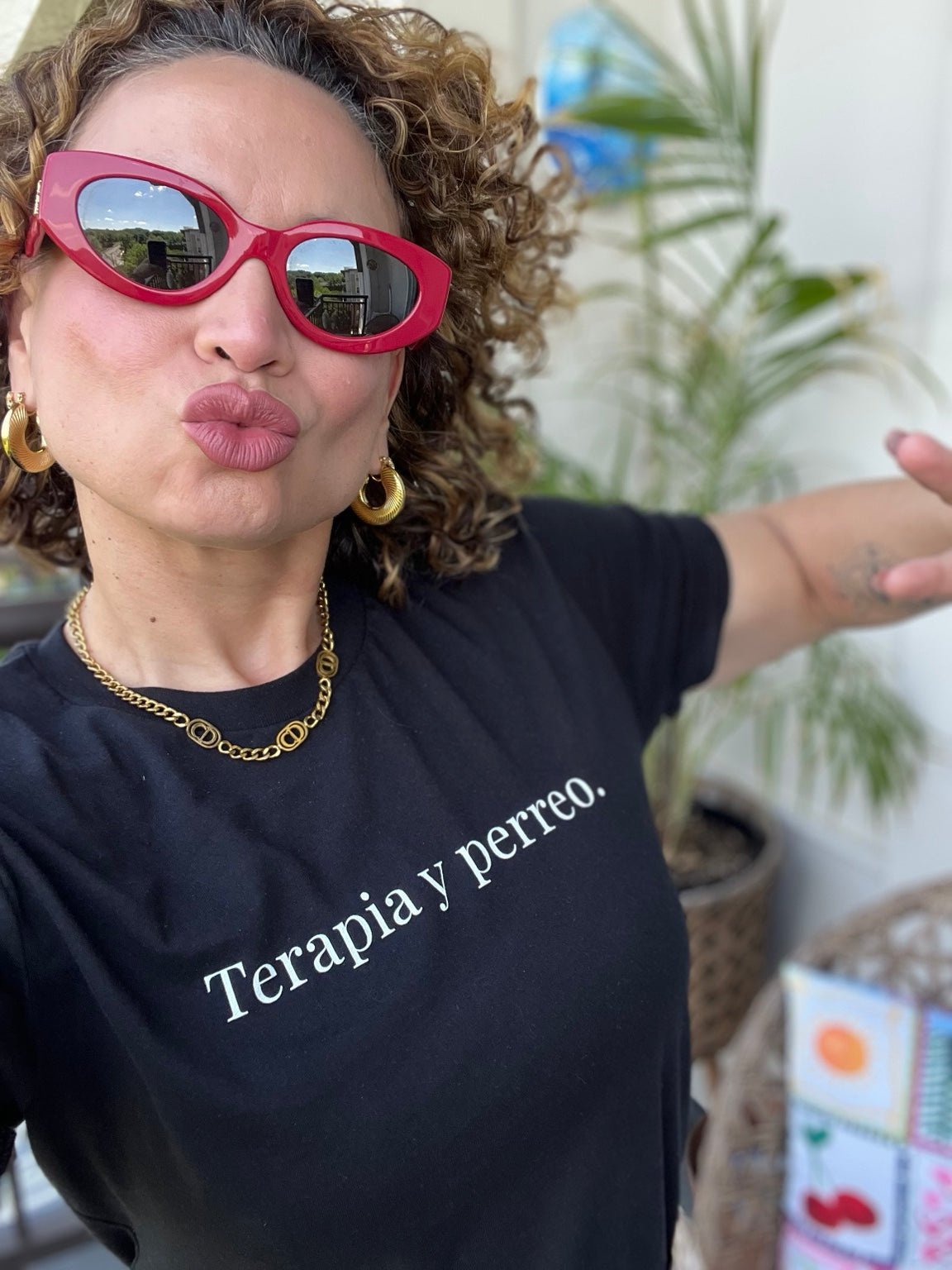Woman wearing the black Terapia y perreo tee with red sunglasses and gold jewelry